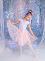 A young girl modeling a light pink and lavender fairy tale-style Barbie tutu dress, posed in a whimsical, snowy studio backdrop with hanging snowflakes and fairy lights.